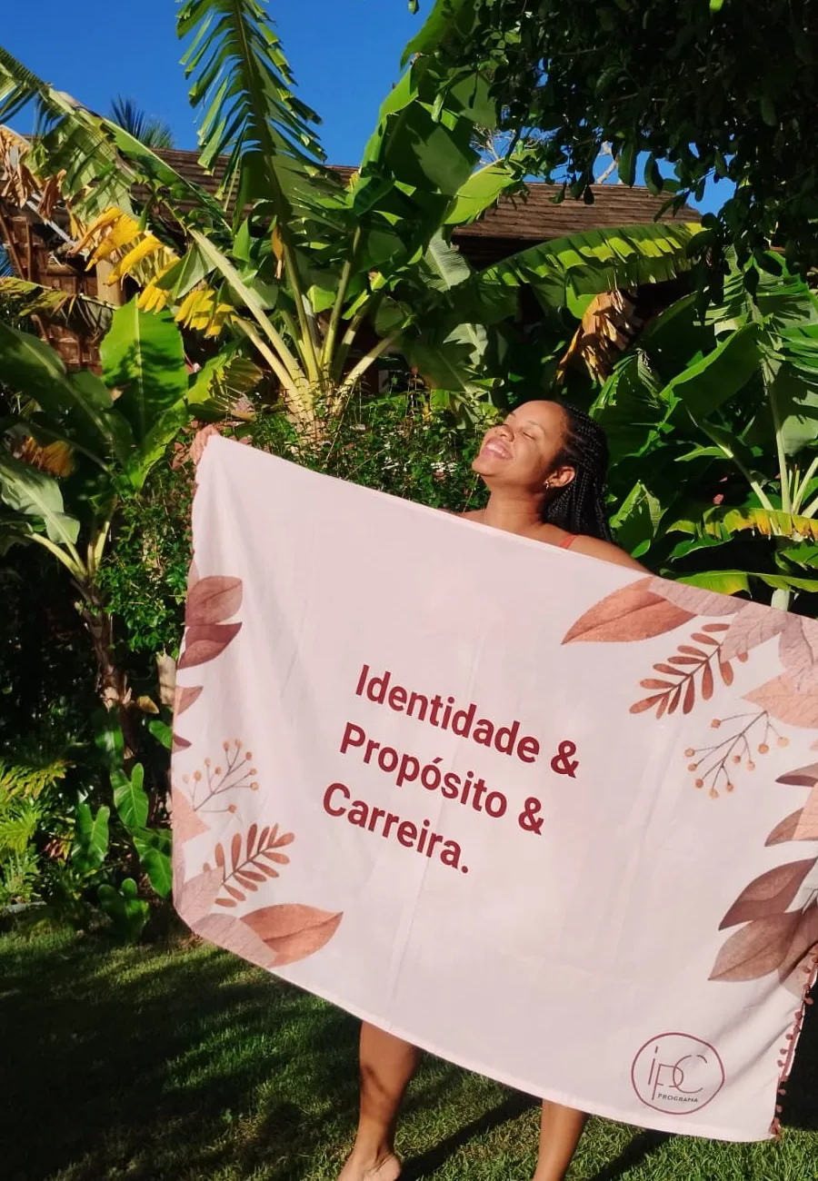 Participante segurando a bandeira Identidade, Propósito e Carreira da Imersão IPC, em meio ao verde