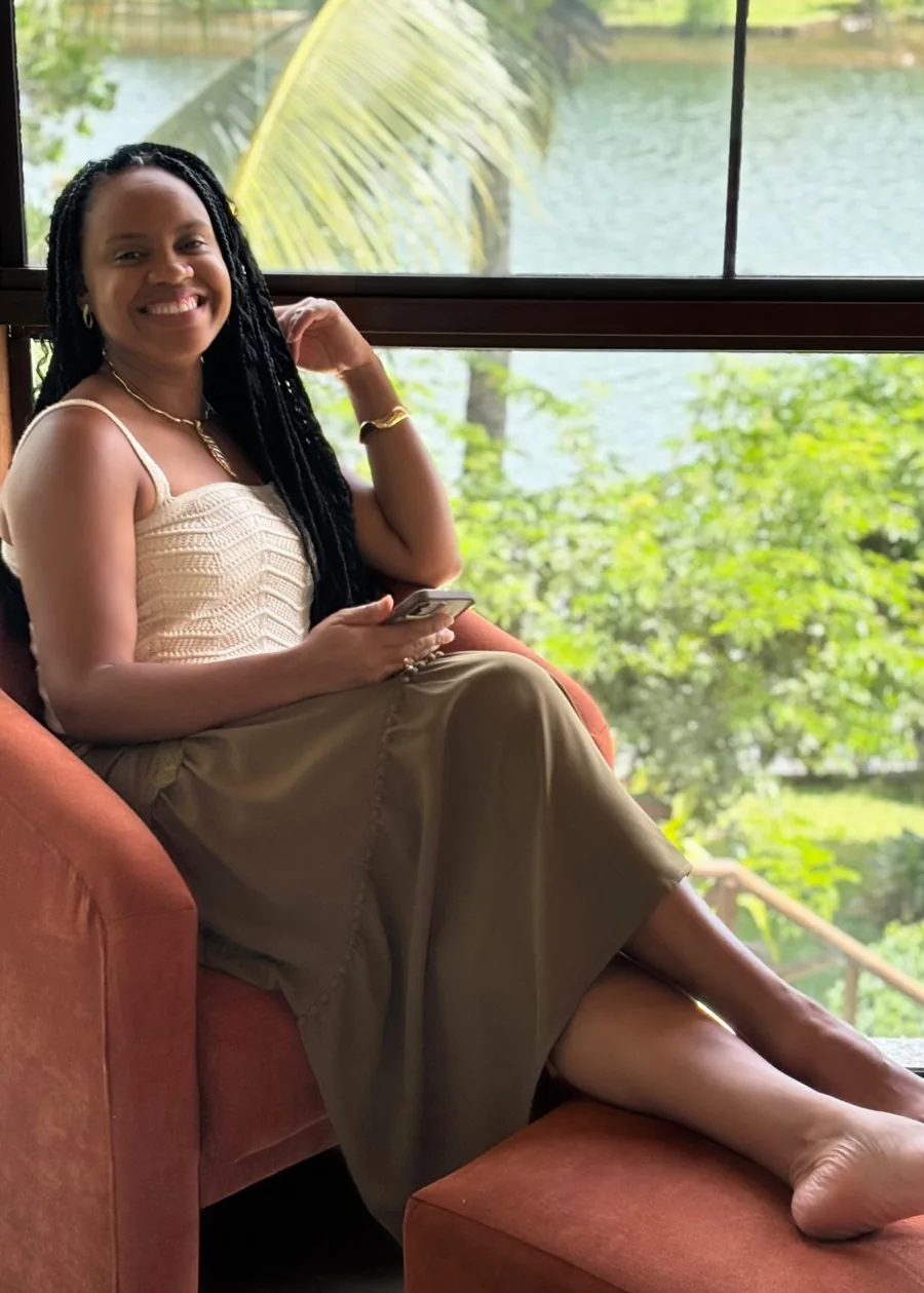 Dalila Garcez sentada em uma poltrona, sorrindo, com a lagoa ao fundo